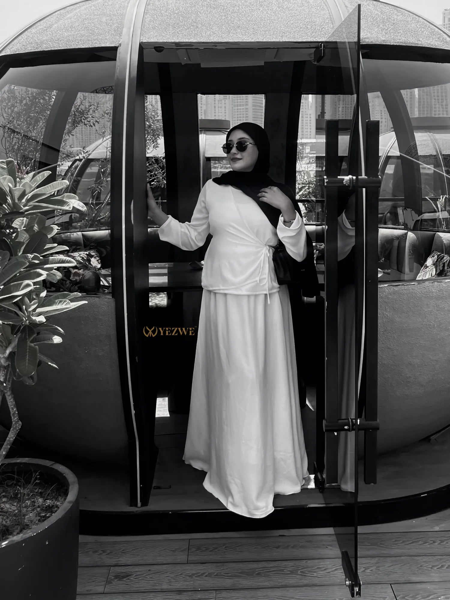 Woman wearing YEZWE white Co-Ord set with a hijab and sunglasses standing at glass door entrance