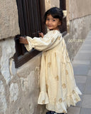 little girl wearing cream embroidered ethnic dress looking back while standing near window side back view candid shot