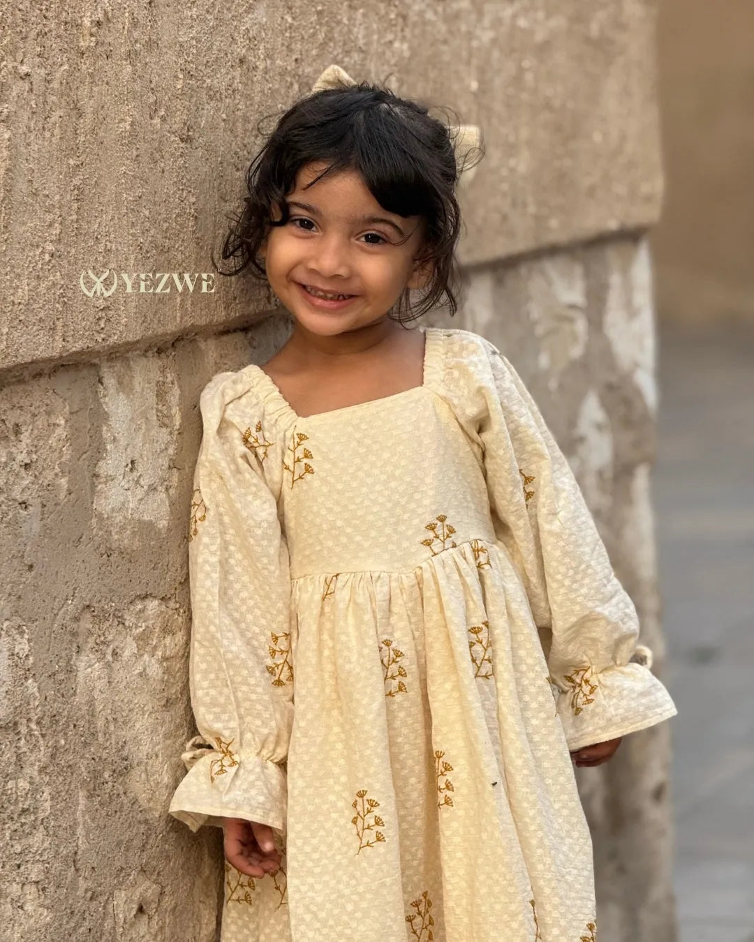 smiling little girl wearing cream embroidered ethnic dress standing near wall close up portrait