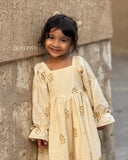 smiling little girl wearing cream embroidered ethnic dress standing near wall close up portrait