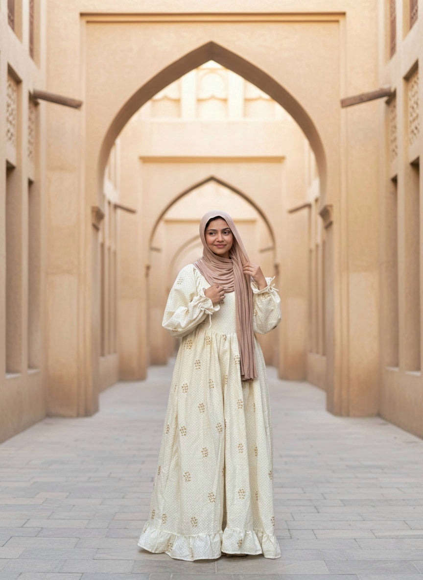 young woman wearing cream embroidered modest maxi dress with hijab standing under archway full length view