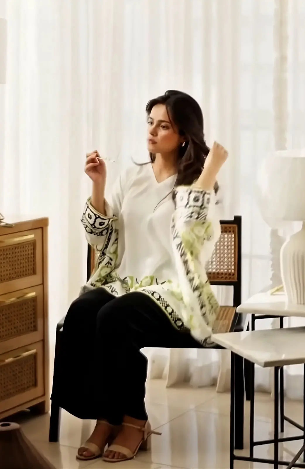 woman wearing cream printed modest top with black pants sitting indoors in a minimal lifestyle setting