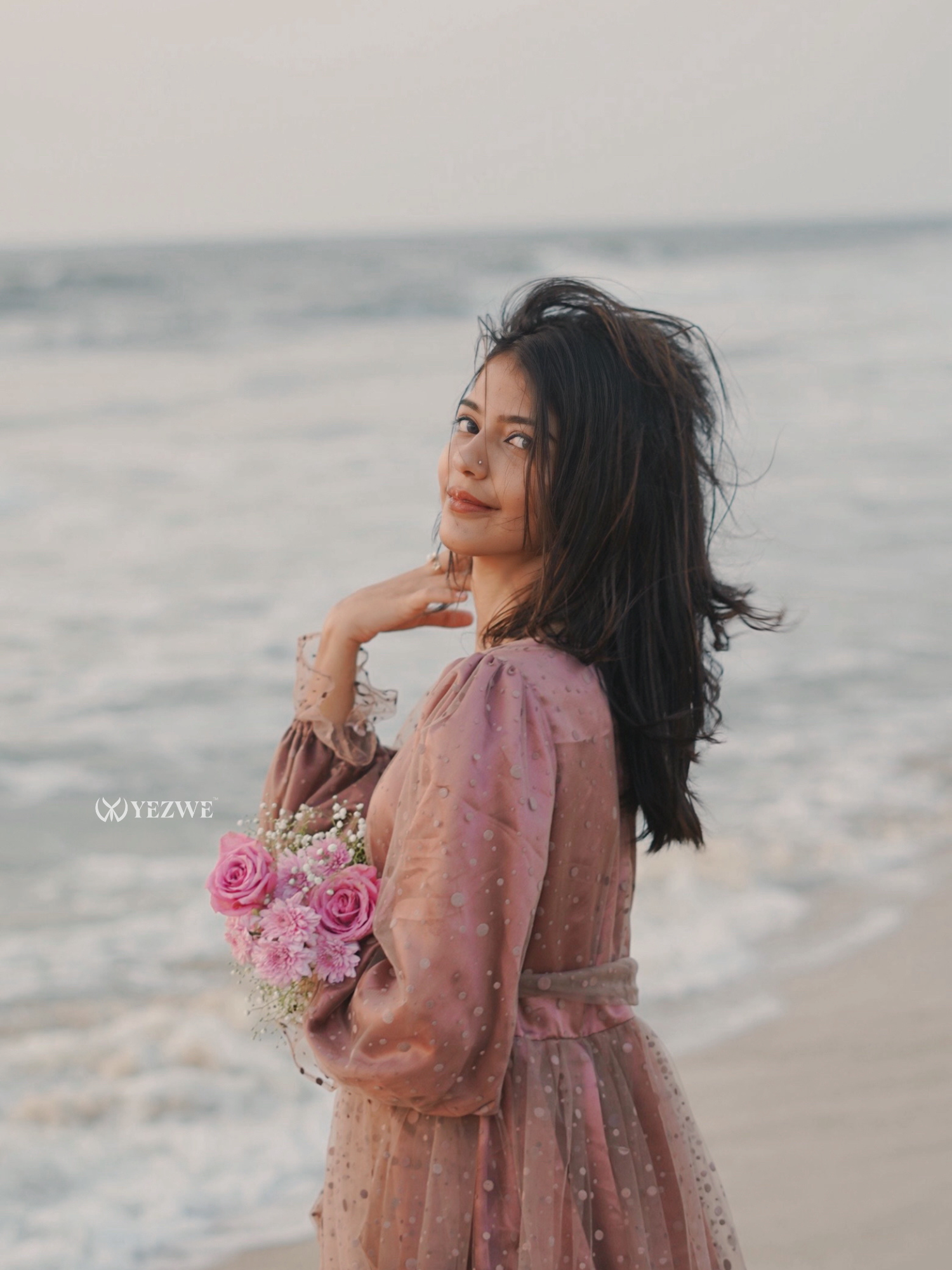 Elegant Yezwe dusty rose modest gown worn by a woman on the beach holding pink roses