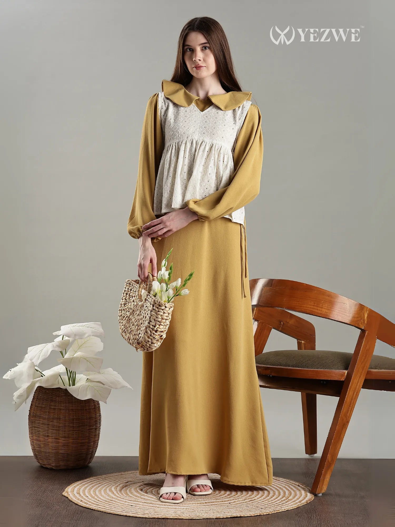 Golden Modest Maxi Dress with Hakoba Shrug by YEZWE shown on woman carrying woven bag standing next to wooden chair
