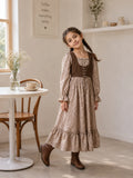 Young girl wearing a beige floral Linen Lux maxi dress with brown corduroy bodice and boots in a bright café-inspired indoor setting.
