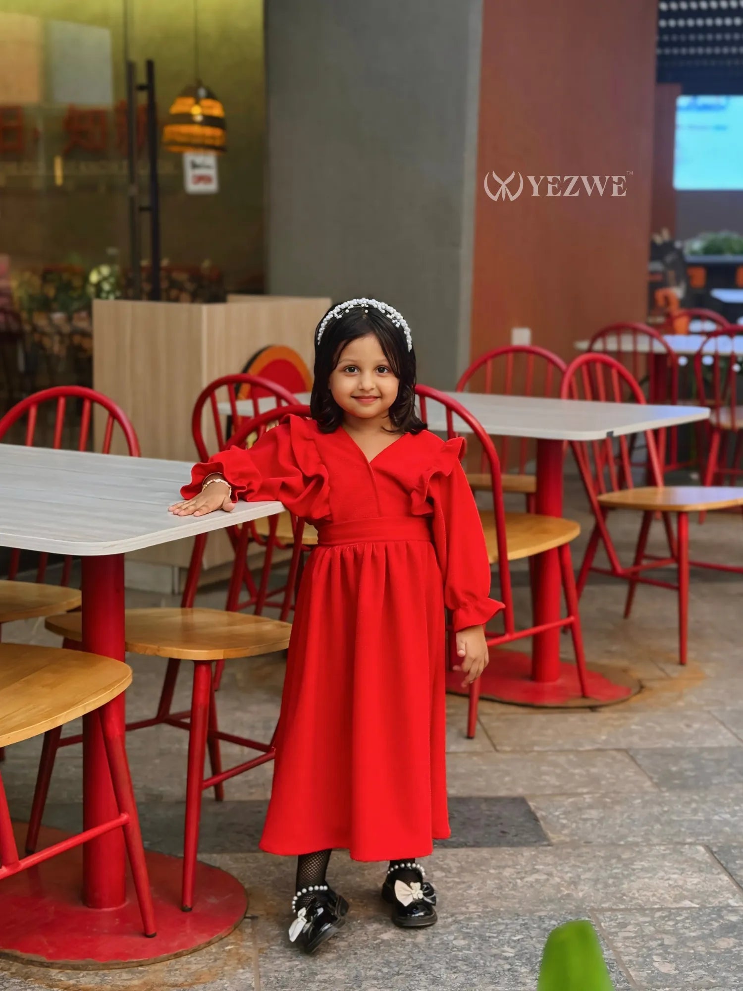 Junior girl in red YEZWE maxi dress for junior girls standing by table in cafe setting