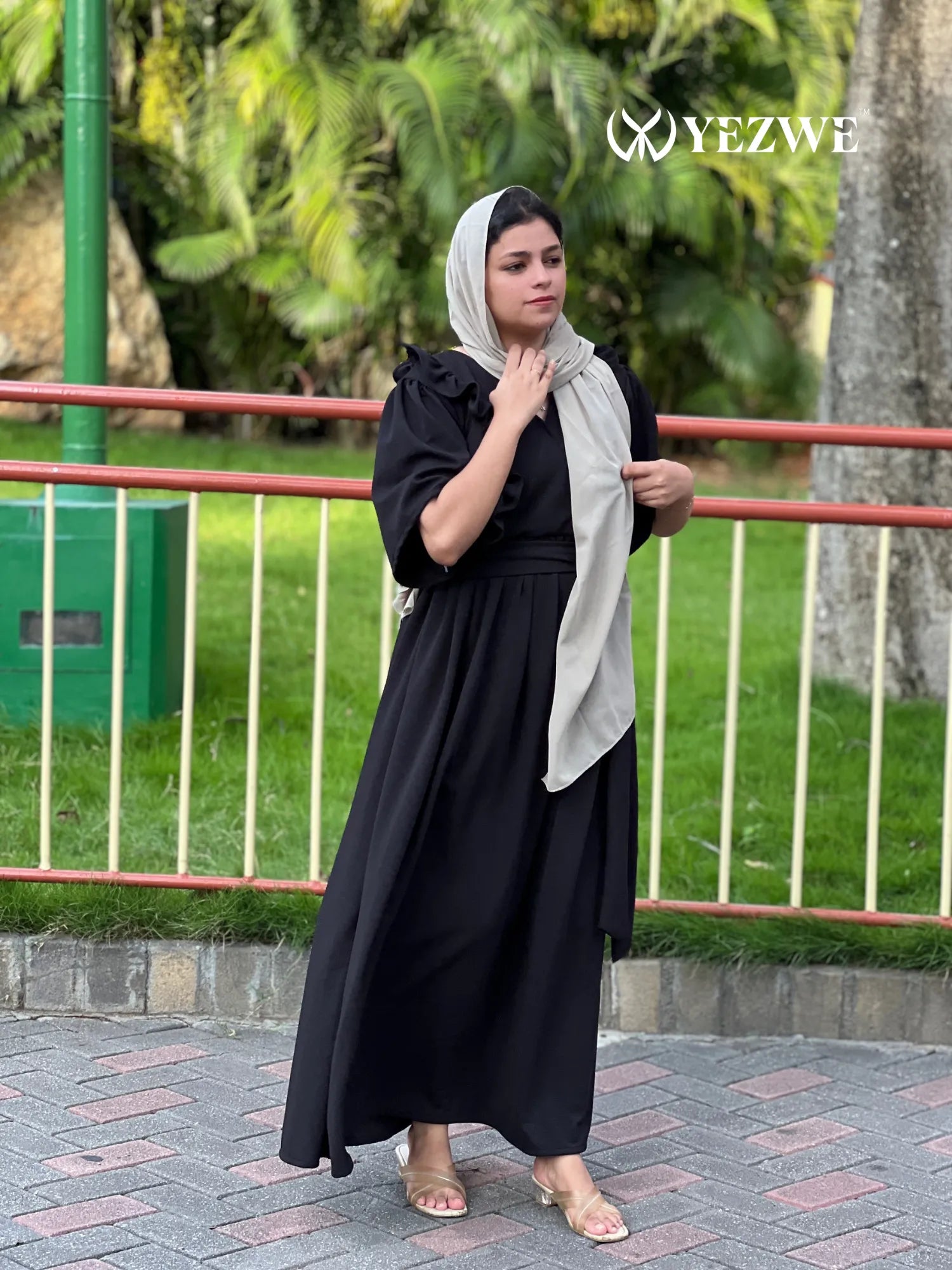 Woman wearing a modest black maxi dress by YEZWE with puff sleeves and a beige headscarf outdoors