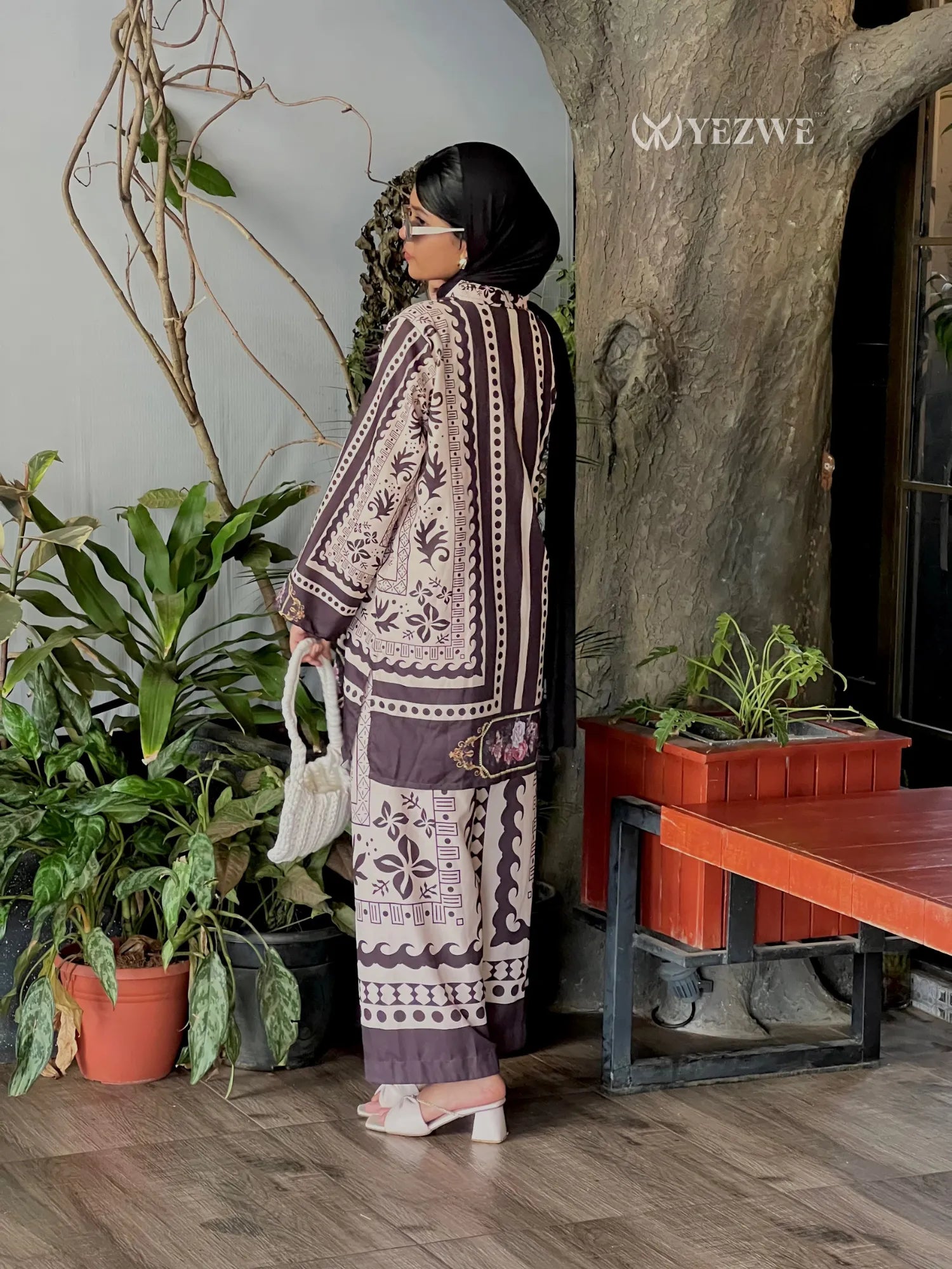 Woman wearing modest ethnic co-ord set with intricate patterns by YEZWE standing indoors near plants and wooden furniture