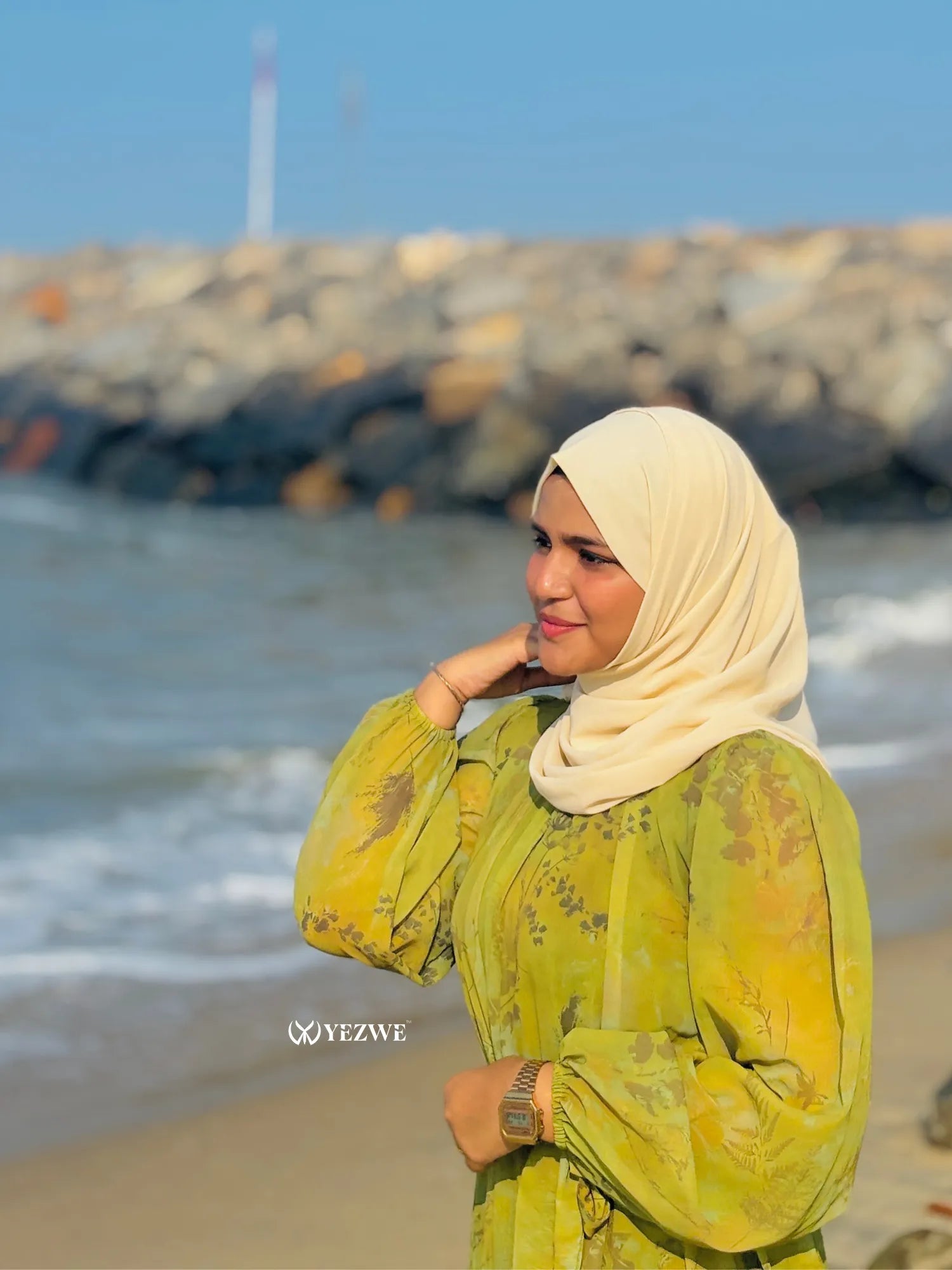 Modest green floral maxi dress by Yezwe worn by a woman on the beach with ocean waves in the background