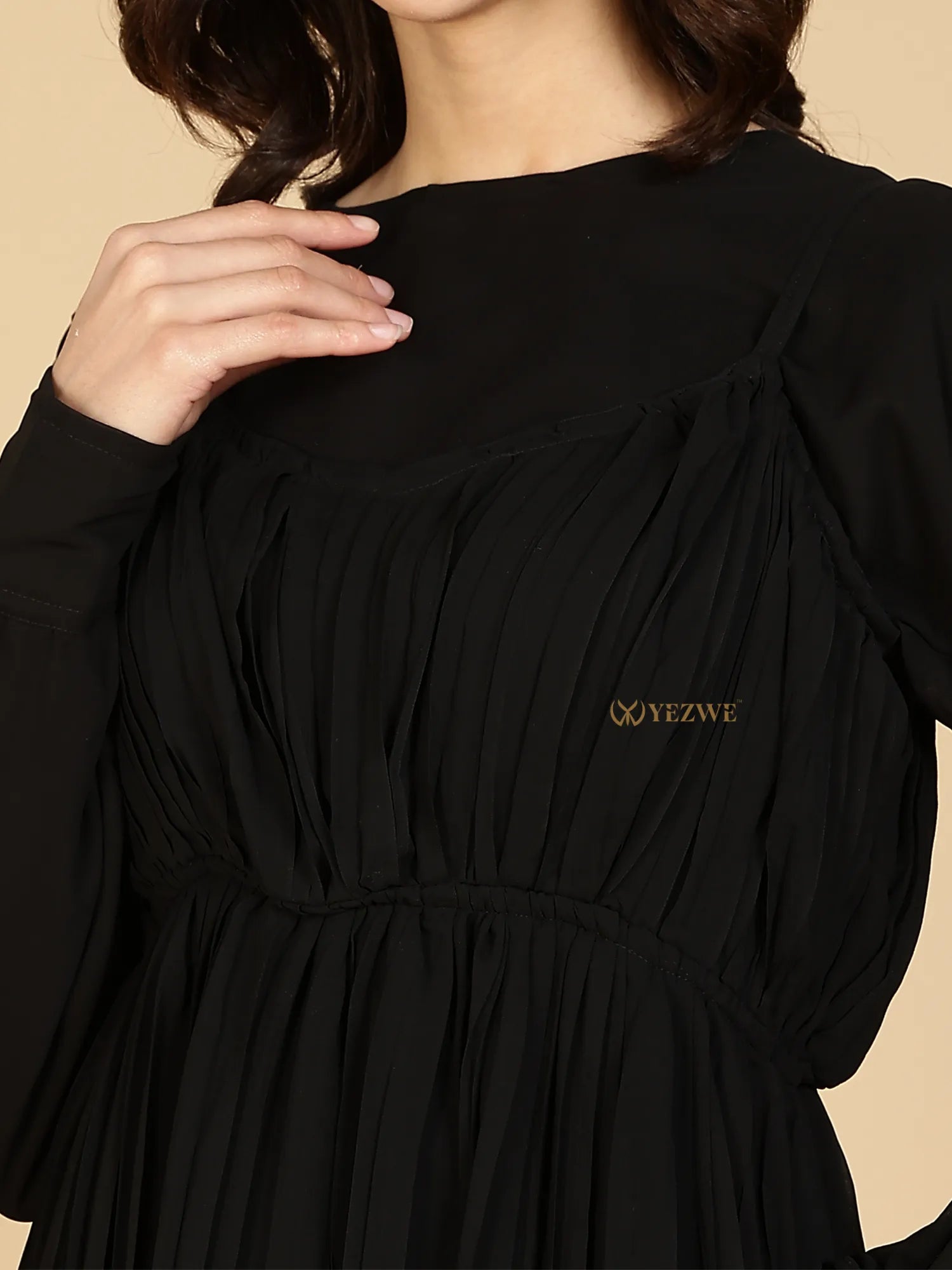 Close up of YEZWE Modest Maxi Dress in black with pleated bodice high neckline long sheer sleeves and gold logo