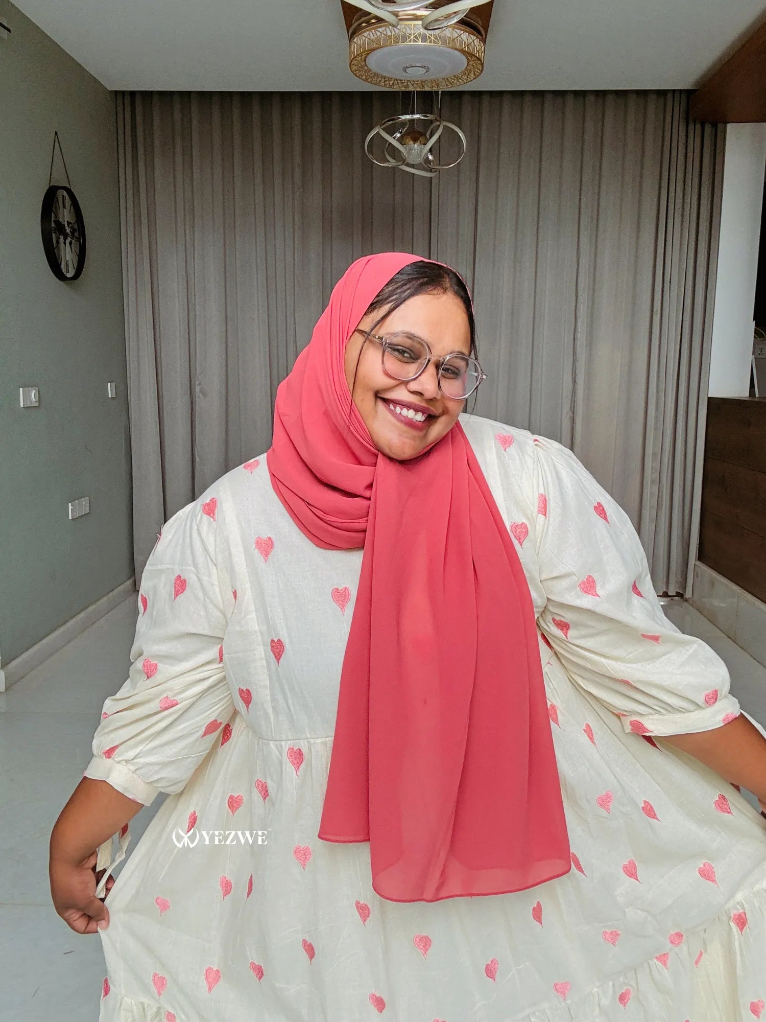 Happy woman wearing a modest pastel pink maxi dress with a matching hijab, smiling in a bright room