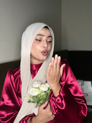 Model wearing a modest rosewood maxi dress with long sleeves and a headscarf, holding white flowers