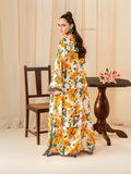 Woman wearing YEZWE Roman Silk Long Tunic with yellow floral print standing next to wooden chair and table