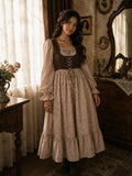 Woman wearing YEZWE vintage floral maxi dress with brown corset-style bodice, puff sleeves, and tiered ruffle hem in a warm vintage-inspired indoor setting.