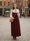young woman wearing a wine maroon modest maxi dress with embroidered yoke and beige hijab standing outdoors near brick wall full length view