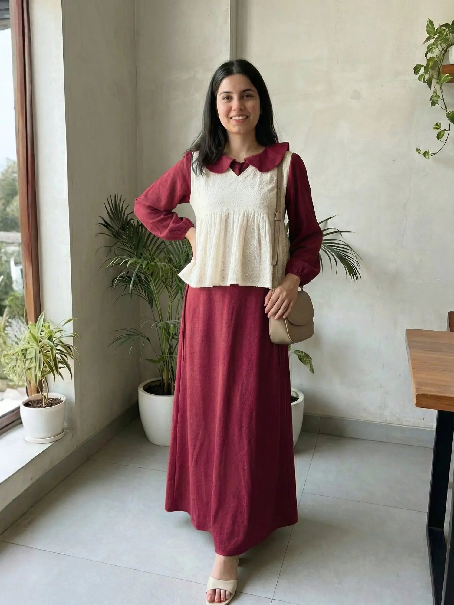 woman wearing wine maroon modest maxi dress with a cream layered sleeveless top standing indoors with a crossbody bag front view