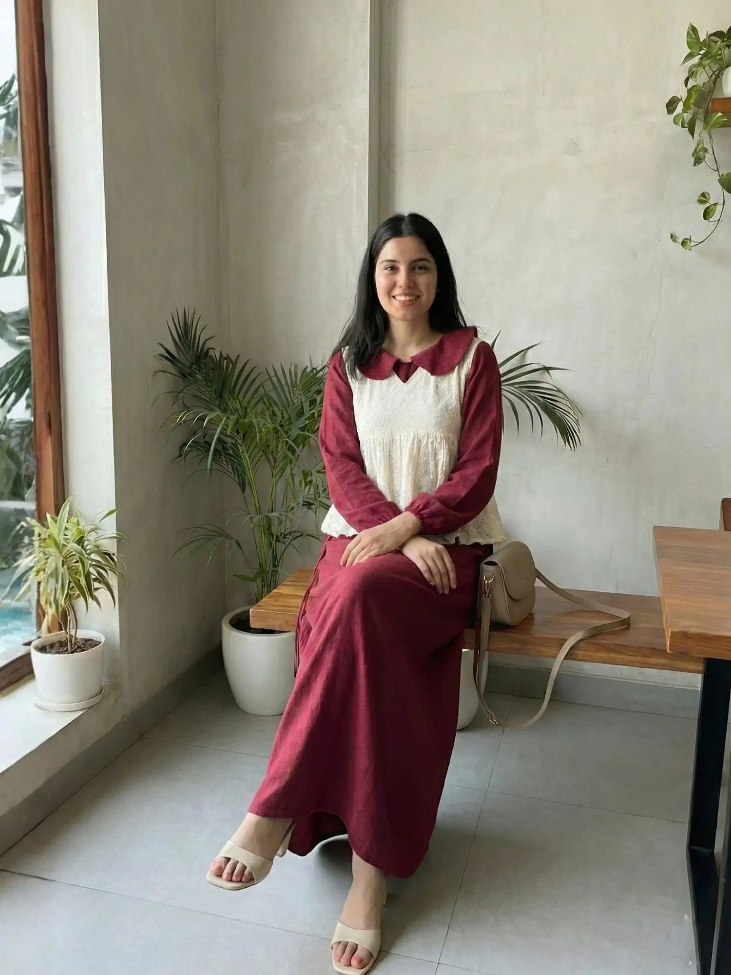 woman wearing wine maroon modest maxi dress with a cream layered sleeveless top sitting indoors in a relaxed lifestyle pose