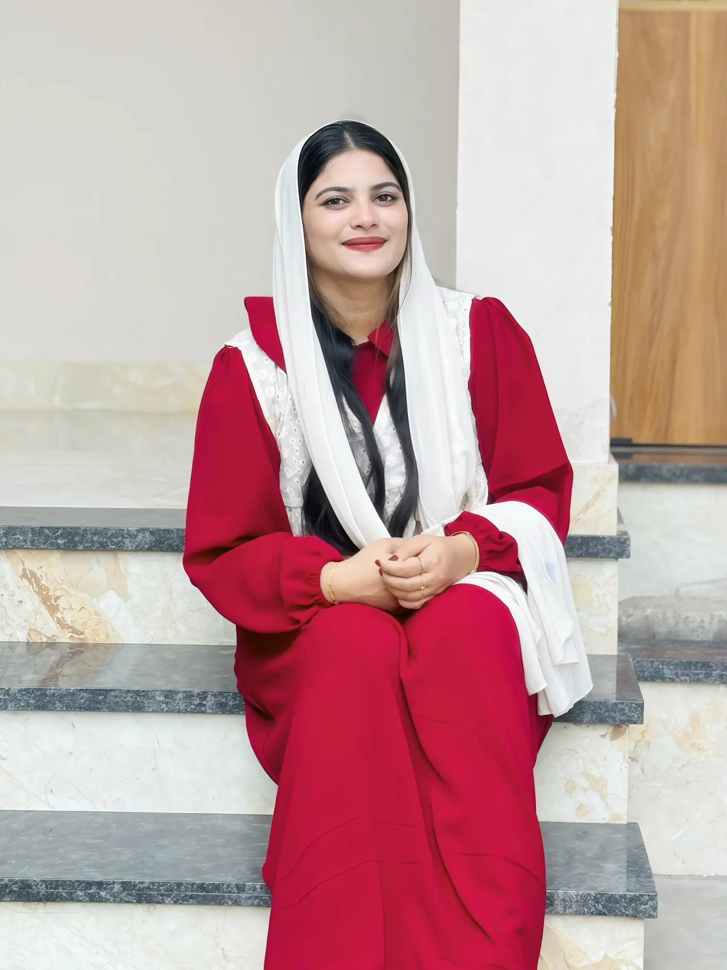 woman wearing wine maroon modest maxi dress with a light dupatta sitting on stairs in a relaxed lifestyle pose