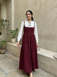 young woman wearing a wine maroon and white layered modest maxi dress walking outdoors near beige wall full length view