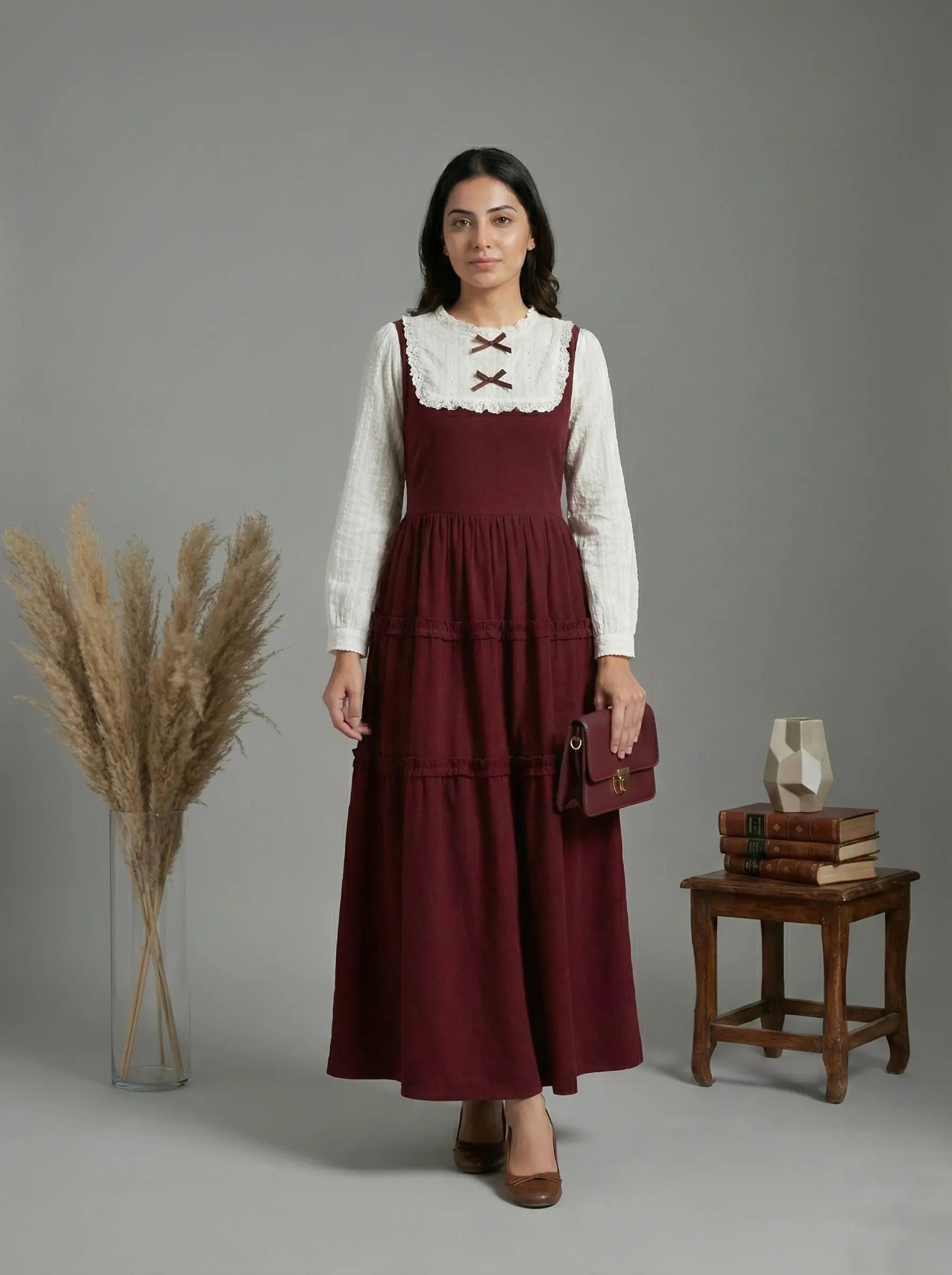 young woman wearing a wine maroon and white layered modest maxi dress standing in studio full length front view holding handbag