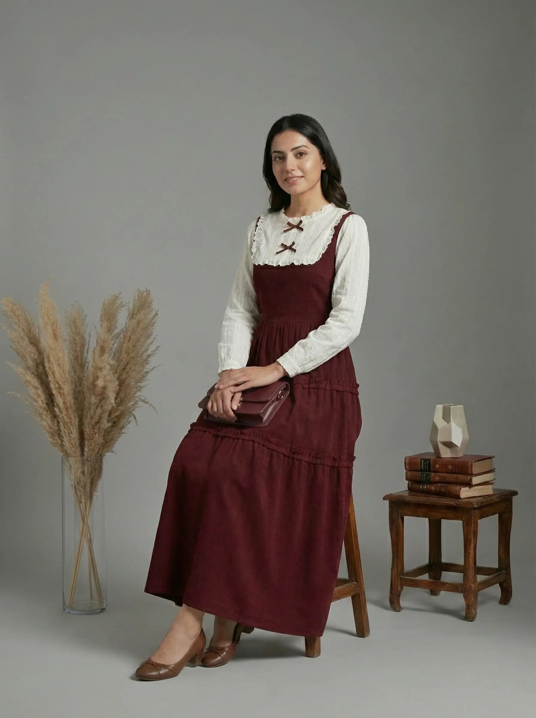 young woman wearing a wine maroon and white layered modest maxi dress sitting on chair in studio setup full length view